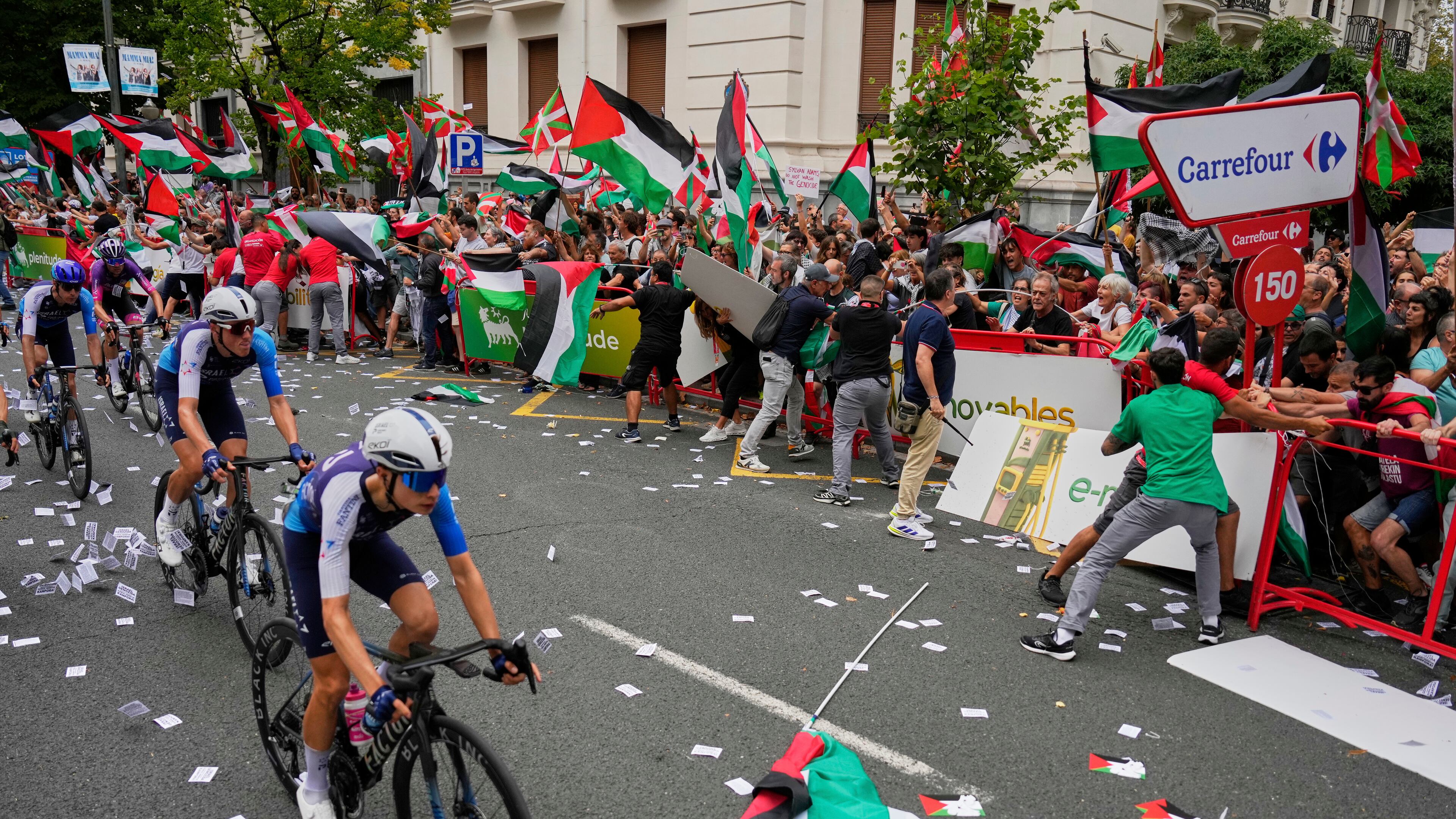 Riders of the Israel Premier Tech team compete as people holding Palestinian flags try to disrupt the eleventh stage of the Spanish Vuelta cycling race, from Bilbao to Bilbao, Spain, Wednesday, Sept. 3, 2025. (AP Photo/Miguel Oses)