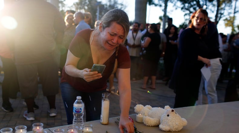A woman places roses on a stage during a vigil at Pine Trails Park for the victims of the Wednesday shooting at Marjory Stoneman Douglas High School in Parkland, Fla., Thursday, Feb. 15, 2018. Nikolas Cruz, accused of using a semi-automatic rifle in a shooting at a Florida high school, confessed to carrying out the killing and carried extra ammunition in his backpack, according to a sheriff's department report released Thursday. (AP Photo/Brynn Anderson)