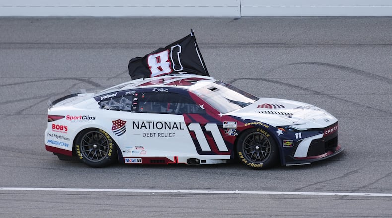 Denny Hamlin celebrates winning while honoring Kyle Busch with a flag after a NASCAR Cup Series auto race at Michigan International Speedway in Brooklyn, Mich., Sunday, June 7, 2026. (AP Photo/Paul Sancya)