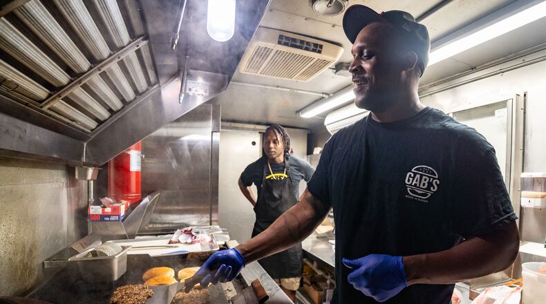 Cornoy Watkins, co-owner of Good As Burgers, prepares vegan burger patties on a grill inside the Good As Burgers food truck outside Bookstore Gallery in Atlanta on Wednesday, July 24, 2024. Due to extreme summer heat, Good As Burgers changed its hours of operation to the evenings. (Seeger Gray / AJC)