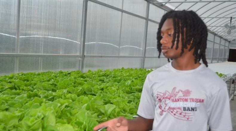 Dougherty High School student Trent McCrary, a summer intern with the Commodore Conyers College & Career Academy Agribusiness Pathway program, explains the process of growing lettuce at the hydroponics greenhouse. (Photo Courtesy of Alan Mauldin)