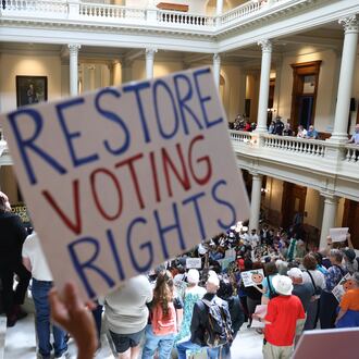 An activist holds a "Restore Voting Rights" sign at a news conference before the state Legislature convenes for a special session at the Capitol on Wednesday. (Arvin Temkar/AJC)