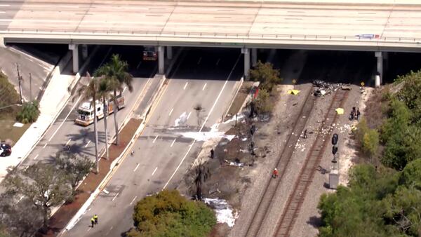 In this image taken from video provided by WSVN-TV, emergency personnel respond to the area where a small plane crashed on the railroad tracks beneath the overpass near Interstate 95 in Boca Raton, Fla., Friday, April 11, 2025. (WSVN-TV via AP)