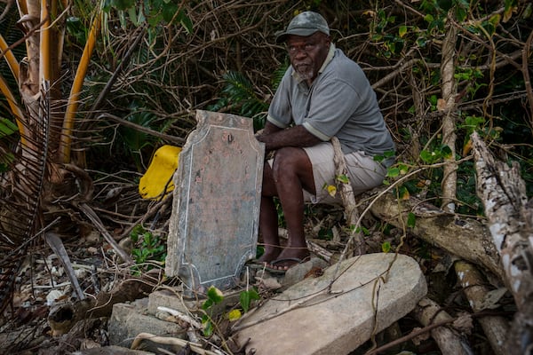 Village chief Amos Kalsont sits at his brother's grave on Pele Island, Vanuatu, just feet from the shoreline, where another headstone has been washed up on top of the site Friday, July 18, 2025. (AP Photo/Annika Hammerschlag)