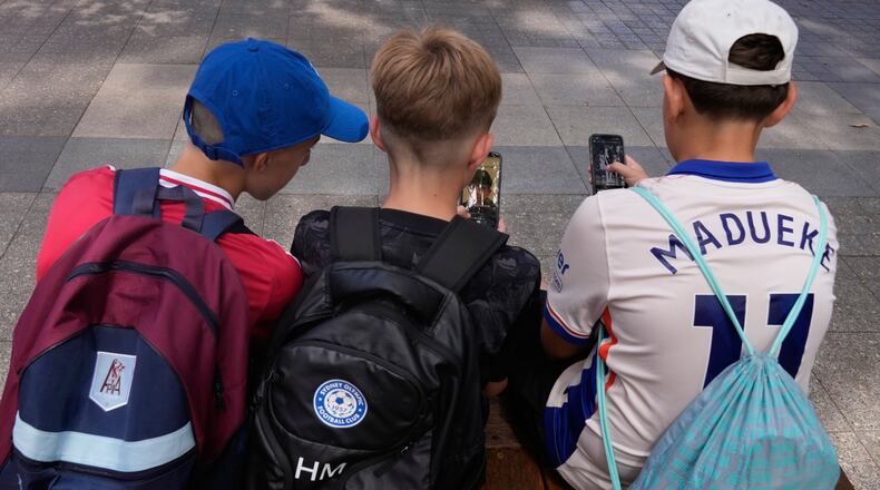 Hugo Winwood-Smith, right, Hardy Macpherson and Edan Abou, left, all 11-years-old, use their phones while sitting outside a school in Sydney, Monday, Dec. 8, 2025. (AP Photo/Rick Rycroft)