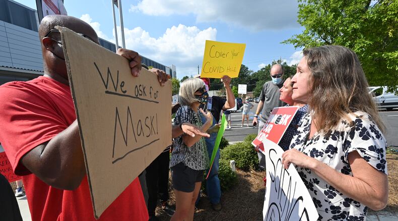 A demonstrator holds a "We ask for mask" sign is confronted outside the headquarters of the Cobb County School District on Aug. 12, 2021.(Hyosub Shin / Hyosub.Shin@ajc.com)