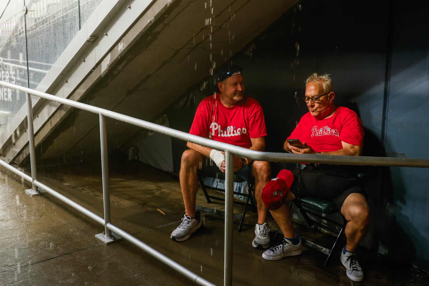 Fans wait under cover during a rain delay before the first inning of the Braves versus Philadelphia Phillies game at Truist Park in Atlanta on Friday, June 27, 2025. (Abbey Cutrer / AJC)