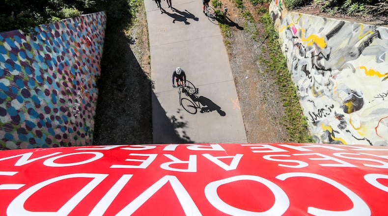 A COVID-19 sign flaps in the wind above people on the Beltline near 10th and Monroe Drive in Atlanta on Friday, May 1, 2020, after Gov. Brian Kemp lifted a shelter-at-home mandate for most Georgians on Thursday, ending the state’s most ambitious attempt to slow the spread of the new coronavirus. JOHN SPINK/JSPINK@AJC.COM