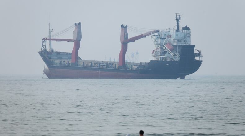 A group of people stands in shallow water as a cargo ship appears anchored in the Strait of Hormuz off Bandar Abbas, Iran, Tuesday, June 30, 2026. (Amirhosein Khorgooi/ISNA via AP)