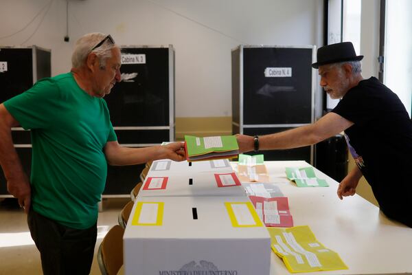 Ballot papers are handed over to a citizen, left, to vote on referendums on citizenship and job protections, at a polling station in Rome, Sunday, June 8, 2025. (Cecilia Fabiano/LaPresse via AP)