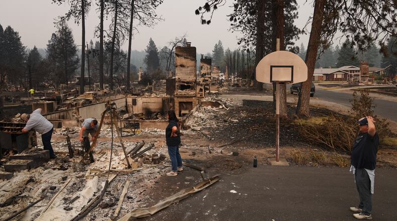 From left, homeowner Al Acosta, his son Louis Acosta, daughter Renee Stewart and son-in-law Jamie Stewart look through the remains of Al's home after a wildfire hit the northern part of Spokane, Wash., Monday, Aug. 3, 2026. (AP Photo/Lindsey Wasson)