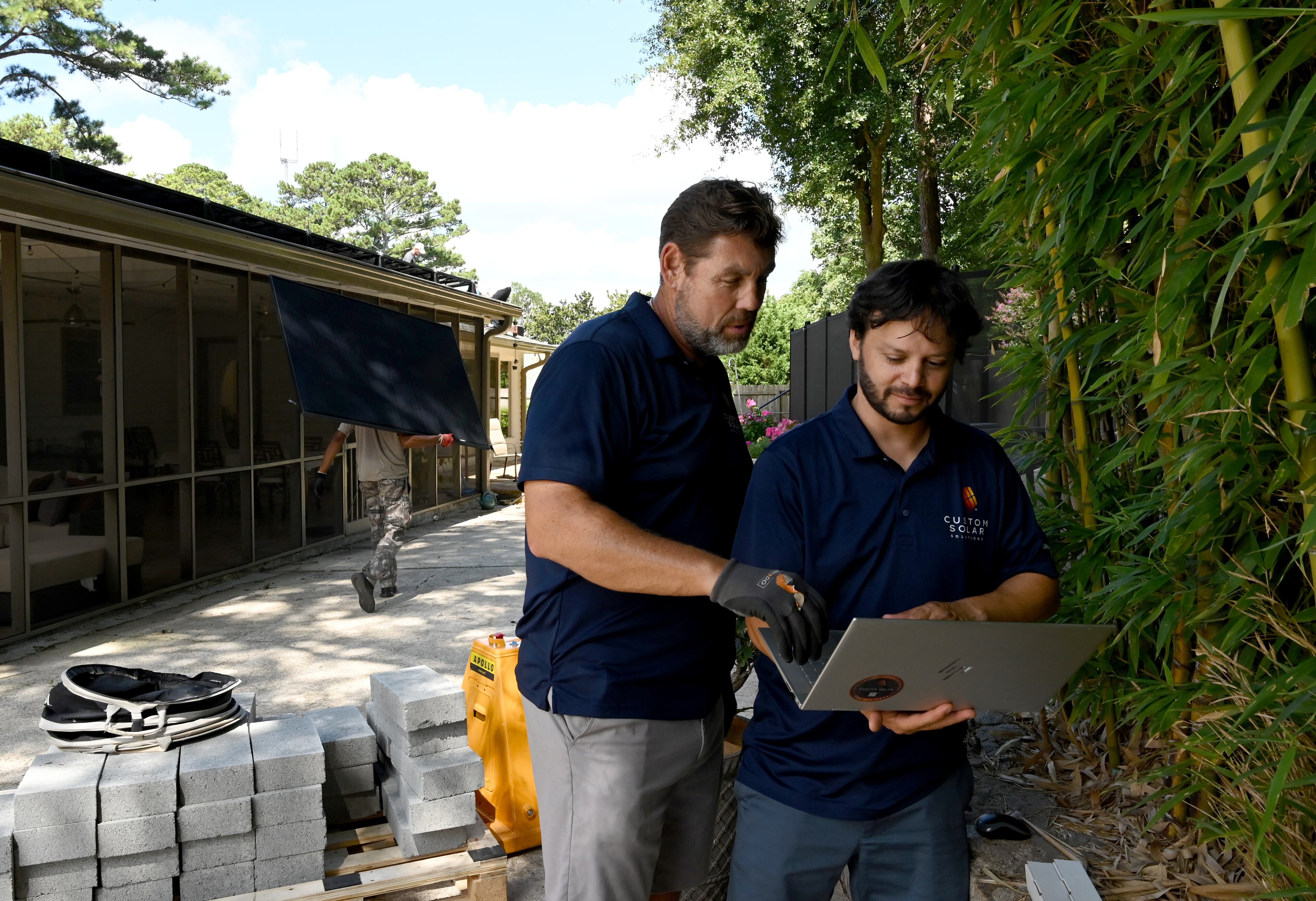 Tom Bowman (left), owner of Custom Solar Solutions, confers with Kareem Bendeck, head of installation, as workers install solar panels on the roof of the Adler family home, Thursday, July 17, 2025, in North Druid Hills. Companies like Custom Solar Solutions, who have already been impacted by tariff-driven cost increases, expect to be hit even harder by the reconciliation bill which eliminates a crucial tax incentive.(Hyosub Shin / AJC)