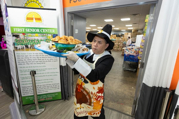 A server wearing a pilgrim costume brings a large platter of food out of the kitchen. (Jason Getz / AJC)