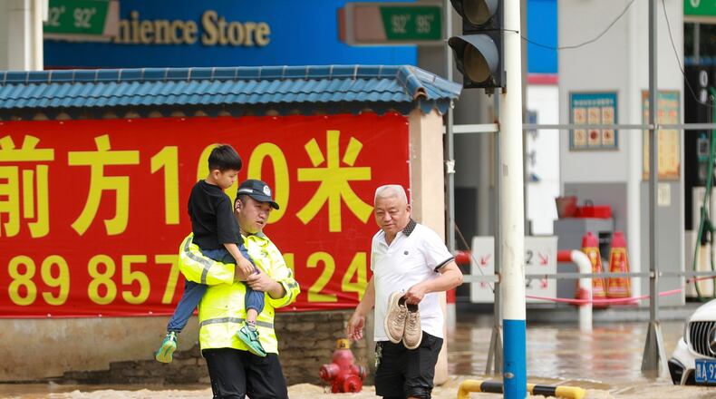 In this photo released by Xinhua News Agency, a police officer holds a boy as he wades through a flooded street in Duyun city, southwestern China's Guizhou Province on Tuesday, May 19, 2026. (Xiao Wei/Xinhua via AP)