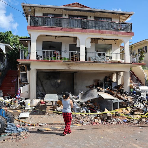 FILE - A woman stands in front of the home where a New Year's Eve firework explosion killed and injured people, Jan. 1, 2025, in Honolulu. (AP Photo/Marco Garcia, File)