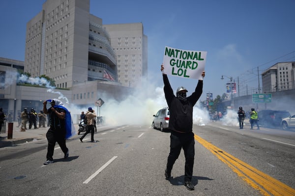 A protester displays a poster as tear gas is used in the metropolitan detention center of downtown Los Angeles, Sunday, June 8, 2025, following last night's immigration raid protest. (AP Photo/Eric Thayer)