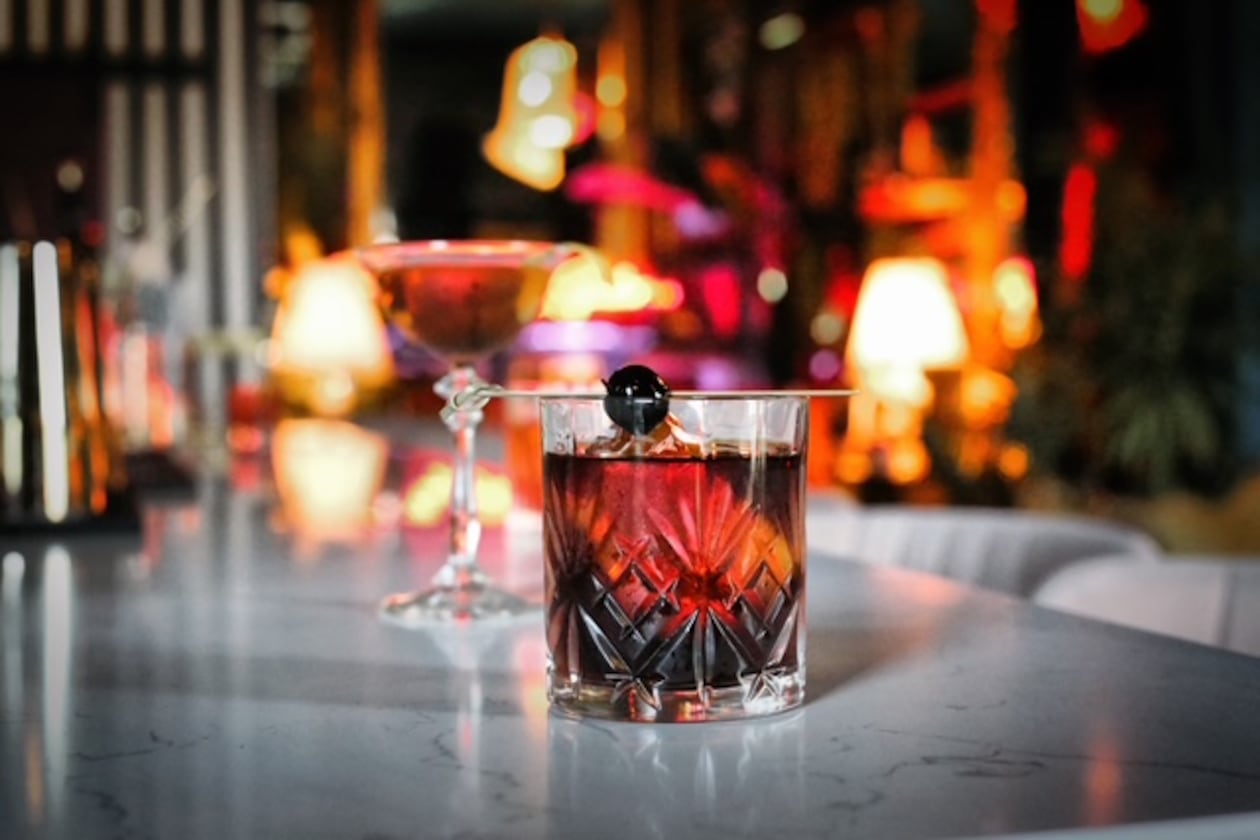 Two cocktails, a Rob Roy and Vieux Carre, placed on a bar. The background of the photo is a blurred image of the lounge.