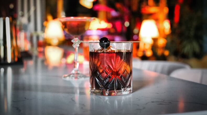 Two cocktails, a Rob Roy and Vieux Carre, placed on a bar. The background of the photo is a blurred image of the lounge.