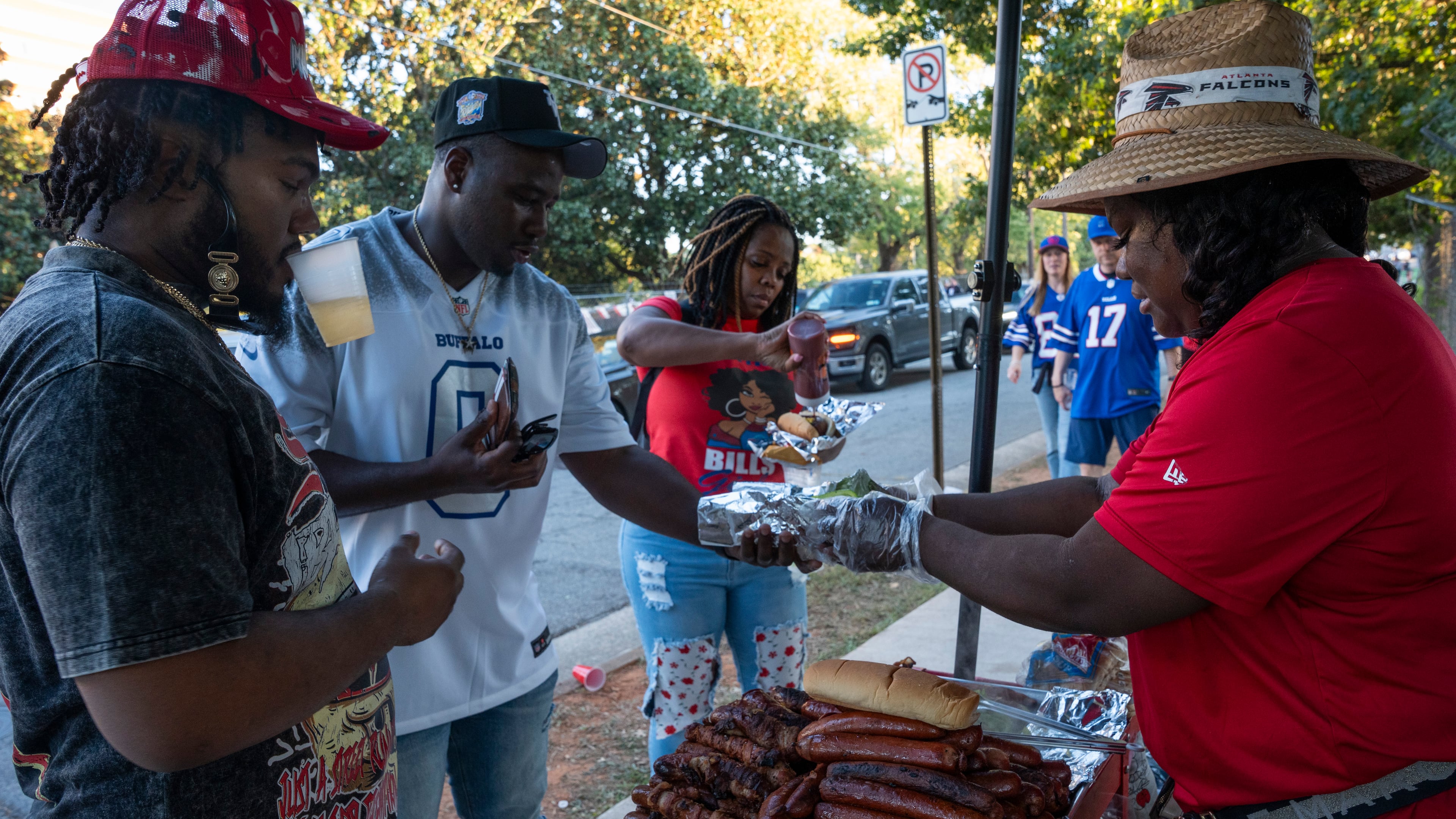Nicole Carswell grills sausages and hot dogs for football fans outside Mercedes-Benz Stadium before the Monday night game between the Buffalo Bills and Atlanta Falcons on Oct. 13, 2025, in Atlanta. Mayor Andre Dickens signed an executive order last month freezing permits for street vendors and community gatherings ahead of the 2026 FIFA World Cup. (Olivia Bowdoin for the AJC)