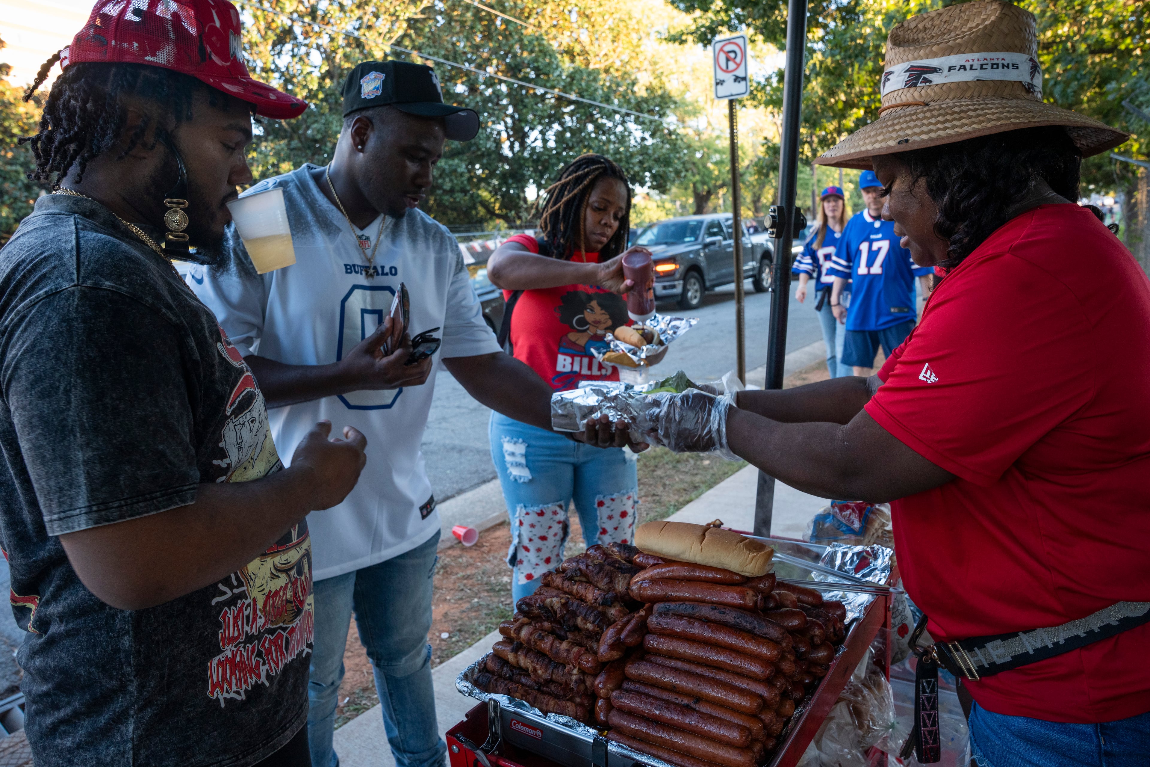 Nicole Carswell grills sausages and hot dogs for football fans outside Mercedes-Benz Stadium before the Monday night game between the Buffalo Bills and Atlanta Falcons on Oct. 13, 2025, in Atlanta. Mayor Andre Dickens recently signed an executive order freezing permits for street vendors and community gatherings ahead of the 2026 FIFA World Cup. (Olivia Bowdoin for The Atlanta Journal-Constitution)
