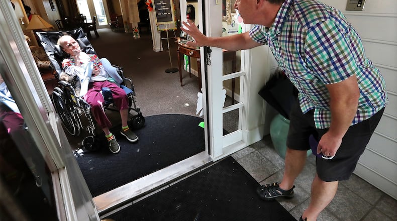 Dan Goerke waves at his wife Denise to get her attention and hopefully a smile by temporarily removing his mask while social distancing from outside during a doorway visit at the Mann House, an Alzheimer's care facility that provides assisted living services on Monday, Aug. 3, 2020, in Sandy Springs. (Curtis Compton ccompton@ajc.com)
