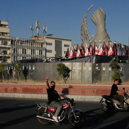 A man reacts to the camera while driving past a monument depicting the clenched fist of the late Iranian Supreme Leader Ayatollah Ali Khamenei, who was killed in the U.S. and Israel strike on Feb. 28, and a missile at the Islamic Revolution square in downtown Tehran, Iran, Tuesday, Sept. 15, 2026. (AP Photo/Vahid Salemi)