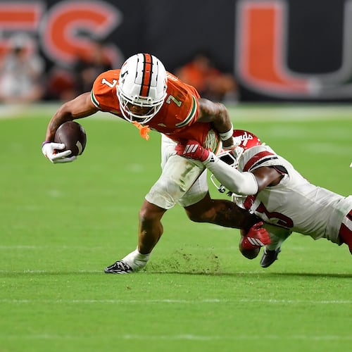 Miami wide receiver CJ Daniels (7) is tackled by Louisville cornerback Justin Agu during the second half of an NCAA college football game, Friday, Oct. 17, 2025, in Miami Gardens, Fla. (AP Photo/Michael Laughlin)