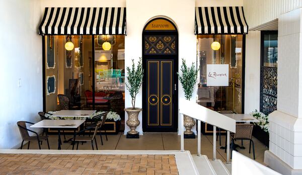 The exterior of.a tea room with striped marquee shades over the windows and a sign that reads Le Faucheur