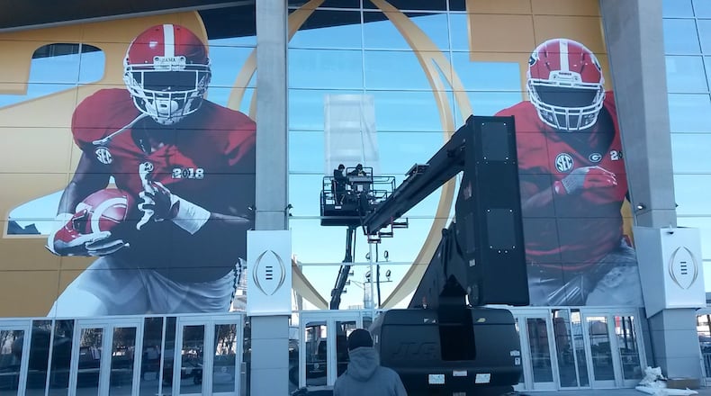 Lots of money has been spent tied to the 2018 national college football championship game in Atlanta. Much of it has been paid to out-of-town companies. Crews installed fresh images on the Mercedes-Benz Stadium on Saturday afternoon in preparation for Monday night’s game. The signs will come down soon after the game. MATT KEMPNER / AJC