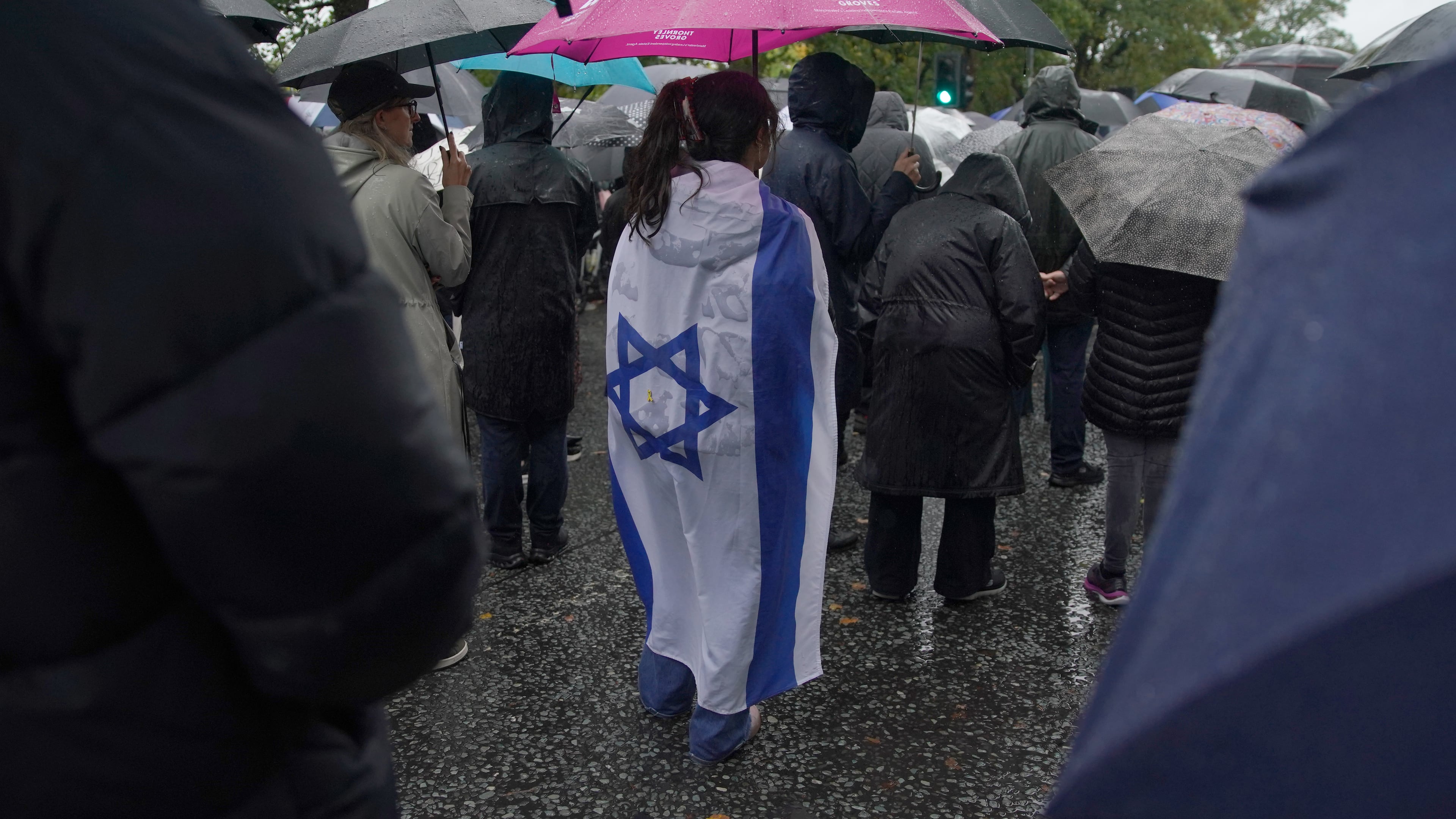 A woman wears the flag of Israel wrapped over her back as she attends a vigil for the victims of the attack on at Heaton Park Hebrew Congregation synagogue, in Crumpsall, Manchester, England, Friday, Oct. 3, 2025. (AP Photo/Ian Hodgson)