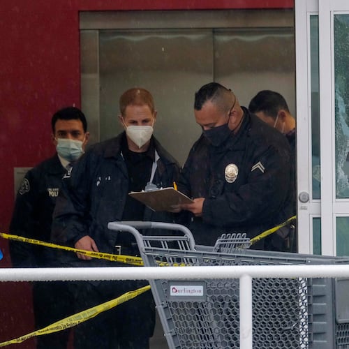 FILE - Police officers work near a broken glass door at the scene where two people were struck by gunfire in a shooting at a Burlington store, Dec. 23, 2021, in North Hollywood, Calif. (AP Photo/Ringo H.W. Chiu, File)
