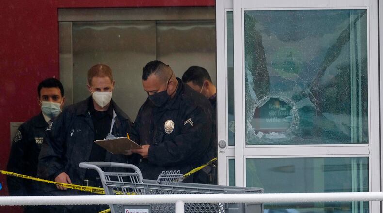 FILE - Police officers work near a broken glass door at the scene where two people were struck by gunfire in a shooting at a Burlington store, Dec. 23, 2021, in North Hollywood, Calif. (AP Photo/Ringo H.W. Chiu, File)