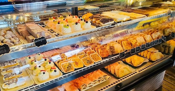 A glass bakery display case shows neat, full rows of desserts, cookies, meat pies, hand pies and sausage rolls.