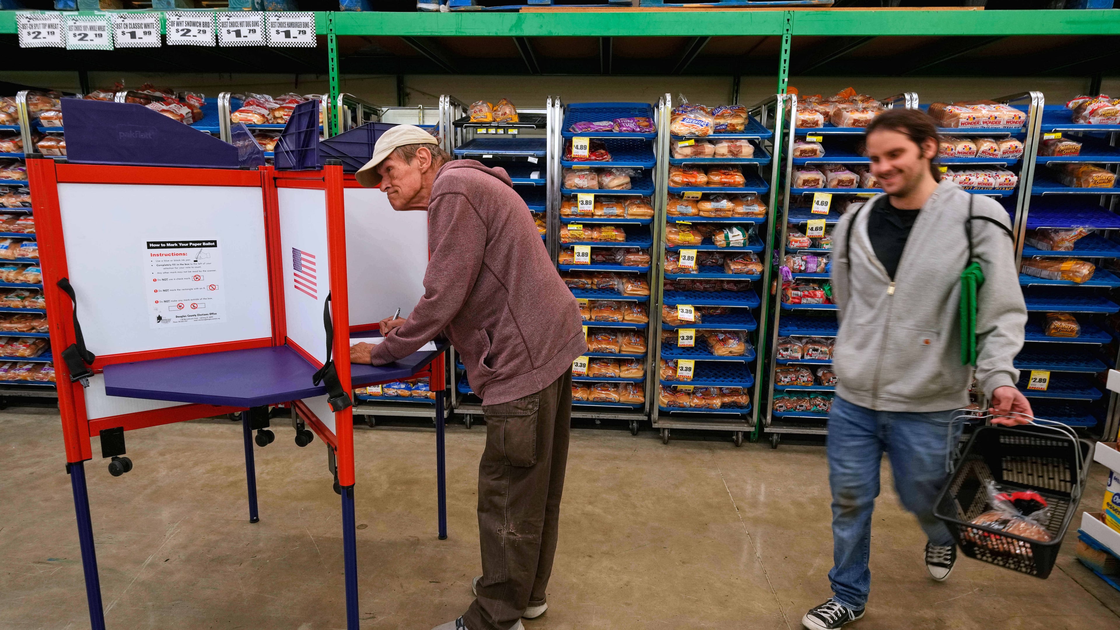 Bob Walser votes while a shopper walks past at the Checkers grocery store in Lawrence, Kan., Tuesday, Nov. 4, 2025. (AP Photo/Charlie Riedel)
