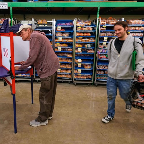 Bob Walser votes while a shopper walks past at the Checkers grocery store in Lawrence, Kan., Tuesday, Nov. 4, 2025. (AP Photo/Charlie Riedel)