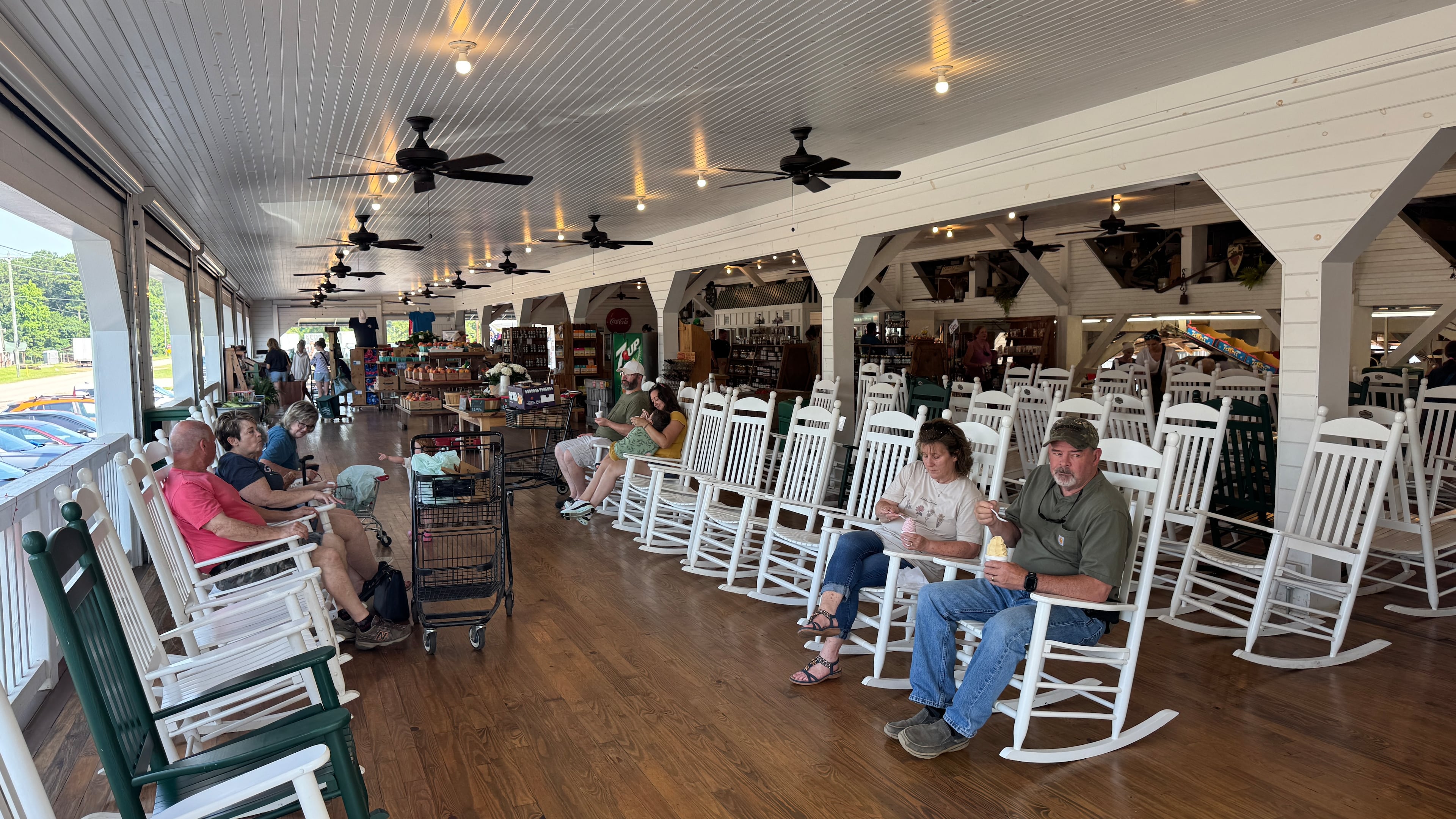 Customers at Dickey Farms relax on rocking chairs in the shade of the peach packinghouse in Musella on Sunday, June 22, 2025. (Joe Kovac Jr./AJC)
