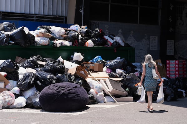 A woman drops off trash at a garbage collection site, Thursday, July 3, 2025, in Philadelphia. (AP Photo/Matt Slocum)