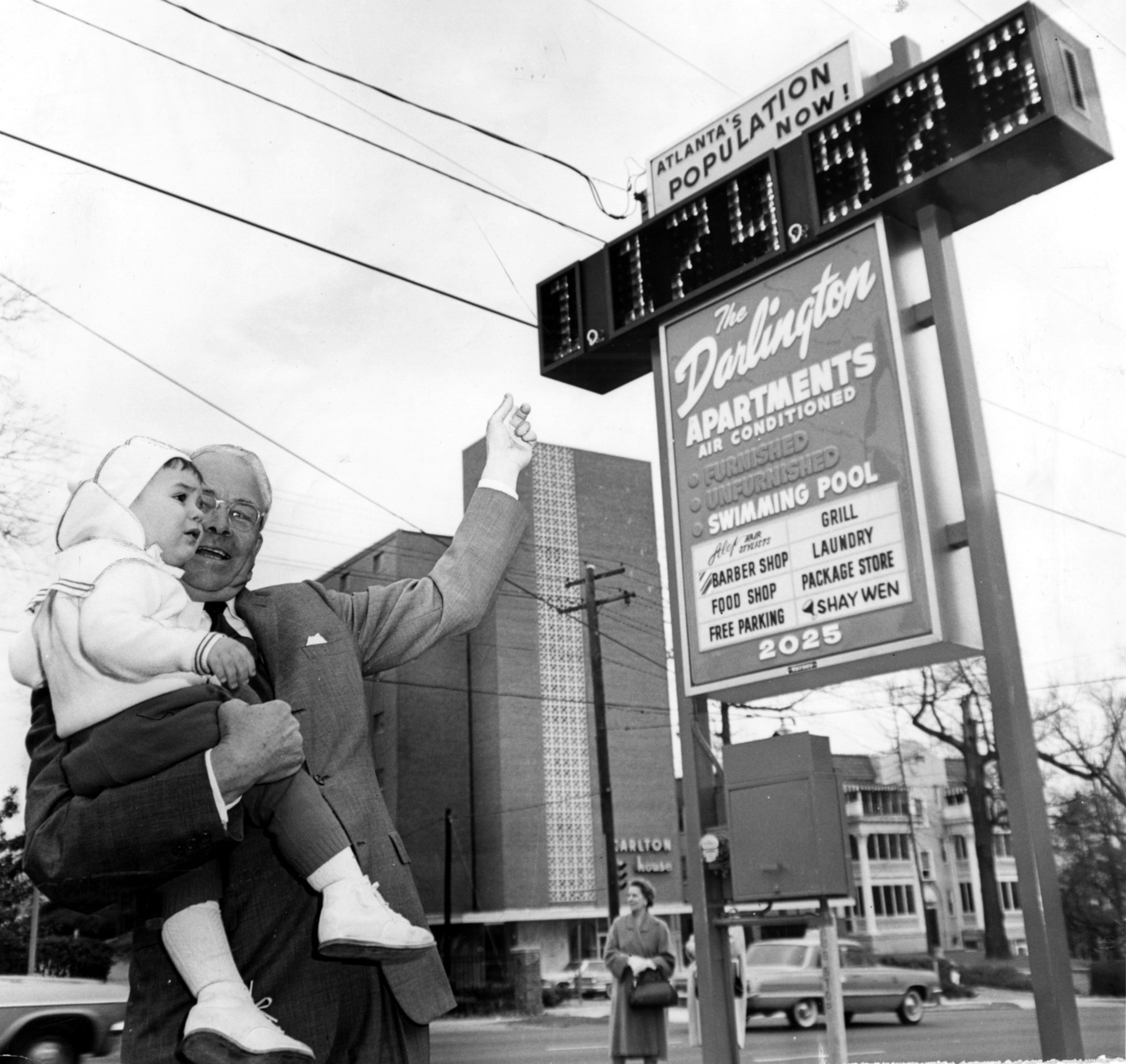 Then-Mayor Ivan Allen Jr.shows (or rather tries to show) Scott Silvis, 16 months, the new electric sign at the Darlington Apartments, 2025 Peachtree Road, that shows a running count of Atlanta's population. Count at 9:30 a.m. Tuesday, March 16, 1965, when the mayor threw the switch was 1, 174,575. The city population was then growing at the rate of one person every 16 minutes. (Charles Pugh/AJC File)