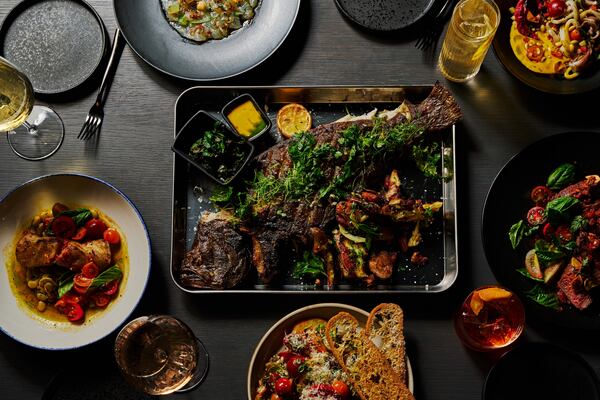Overhead shot of a whole fish with charred skin surrounded by additional plates of food and drinks