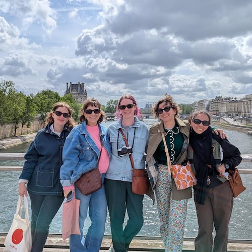 Five women dressed as tourists stand on a bridge in Paris.