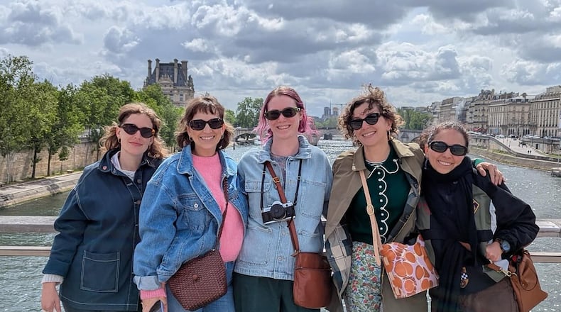 Five women dressed as tourists stand on a bridge in Paris.