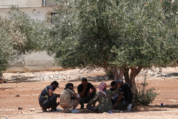 Bedouin fighters sit under the shade of an olive tree outside a temporary shelter housing Bedouin families who fled their homes in Shahba, a town in Syria's southern Sweida province, due to clashes between Bedouin clans and Druze militias, in the town of Nahtah, in the eastern part of Daraa province, Syria, Monday, July 21, 2025. (AP Photo/Omar Sanadiki)