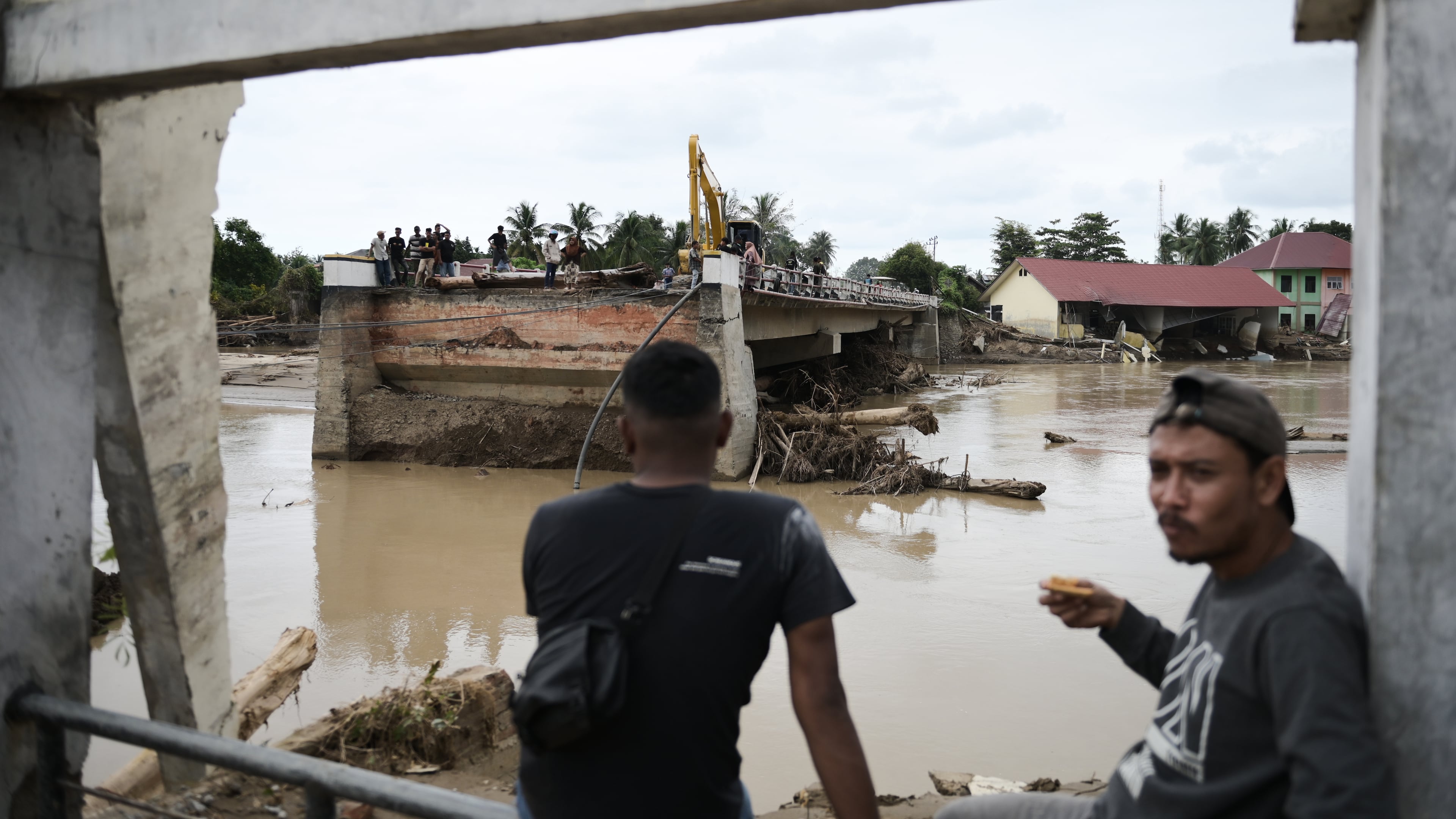 Men sit near a bridge collapsed during a flash flood in Pidie Jaya, Aceh province, Indonesia, Tuesday, Dec. 2, 2025. (AP Photo/Reza Saifullah)