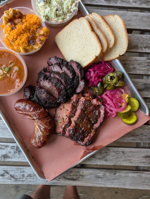 A metal tray filled with three large portions of sliced meats, three side dishes, pickled onions, pickled jalapenos, pickled cucumbers and pickled shallots.
