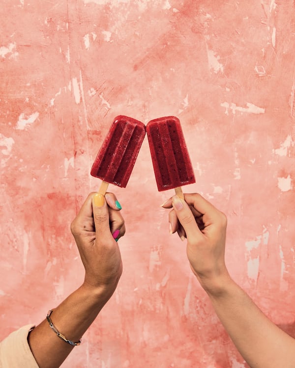 two hands holding one red popsicle each with a pink background