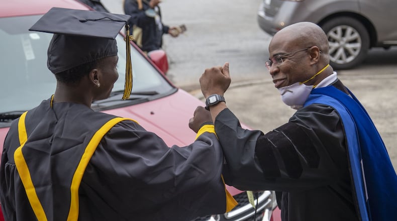 Frederick Douglass High School principal Ellis Duncan (right) congratulates a graduating senior with an elbow bump during a drive-thru celebration event at the school in Atlanta's Center Hill community, Wednesday, May 20, 2020. Graduating seniors were given their diplomas, cap, gowns and academic and athletic awards during the drive-thru event at the school. Students were also given a chance to be photographed win their cap and gown which was provided by the Frederick Douglass High School Alumni Association.