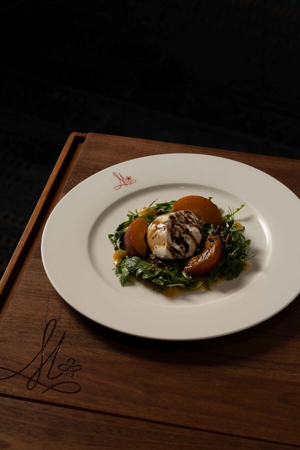 A plate filled with artfully arranged lettuce, topped with peaches and a ball of burrata, all drizzled with balsamic vinaigrette.