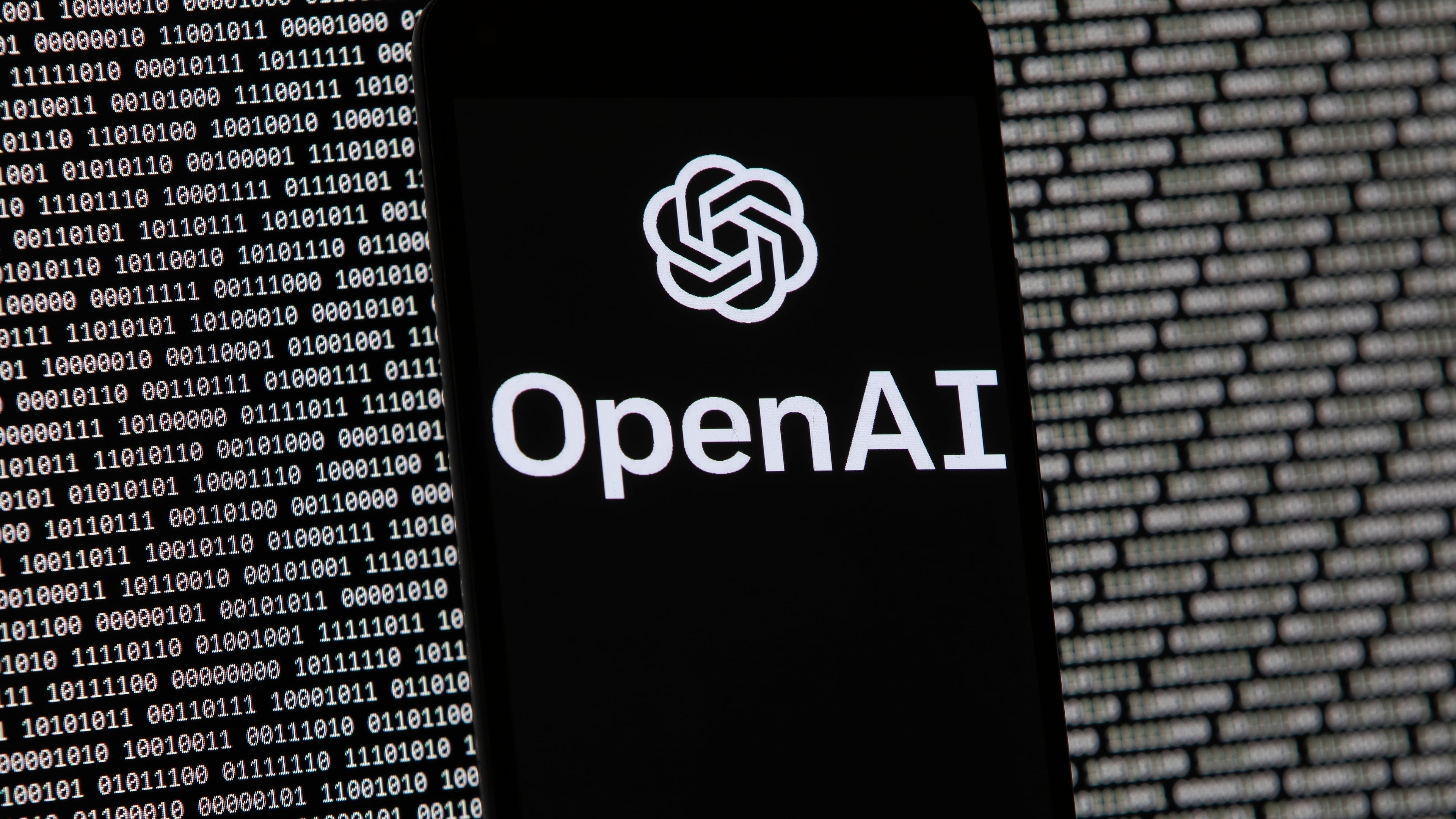 FILE - The OpenAI logo appears on a mobile phone in front of a computer screen with random binary data, March 9, 2023, in Boston. (AP Photo/Michael Dwyer, File)