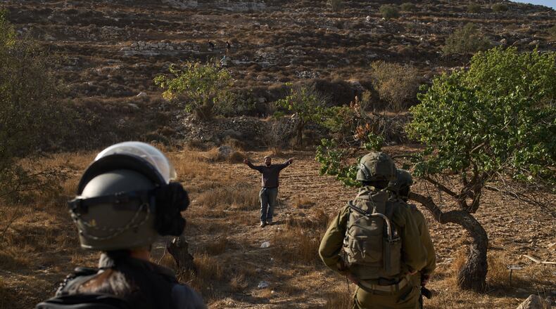 An Israeli settler gestures as Israeli soldiers block access for Palestinians to an area for harvesting olives in the West Bank village of Sa'ir, near Hebron, Thursday, Oct. 23, 2025. (AP Photo/Leo Correa)