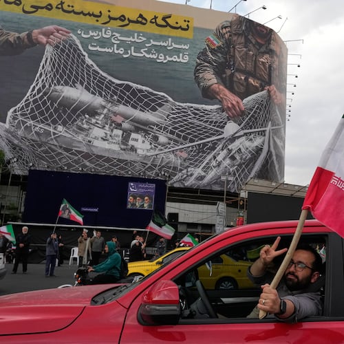 A man flashes a victory sign as he carries an Iranian flag in front of an anti-U.S. billboard depicting the American aircrafts into the Iranian armed forces fishing net with signs that read in Farsi: "The Strait of Hormuz will remain closed, The entire Persian Gulf is our hunting ground," at the Eqelab-e-Eslami, or Islamic Revolution Square in downtown Tehran, Iran, Monday, April 13, 2026. (AP Photo/Vahid Salemi)